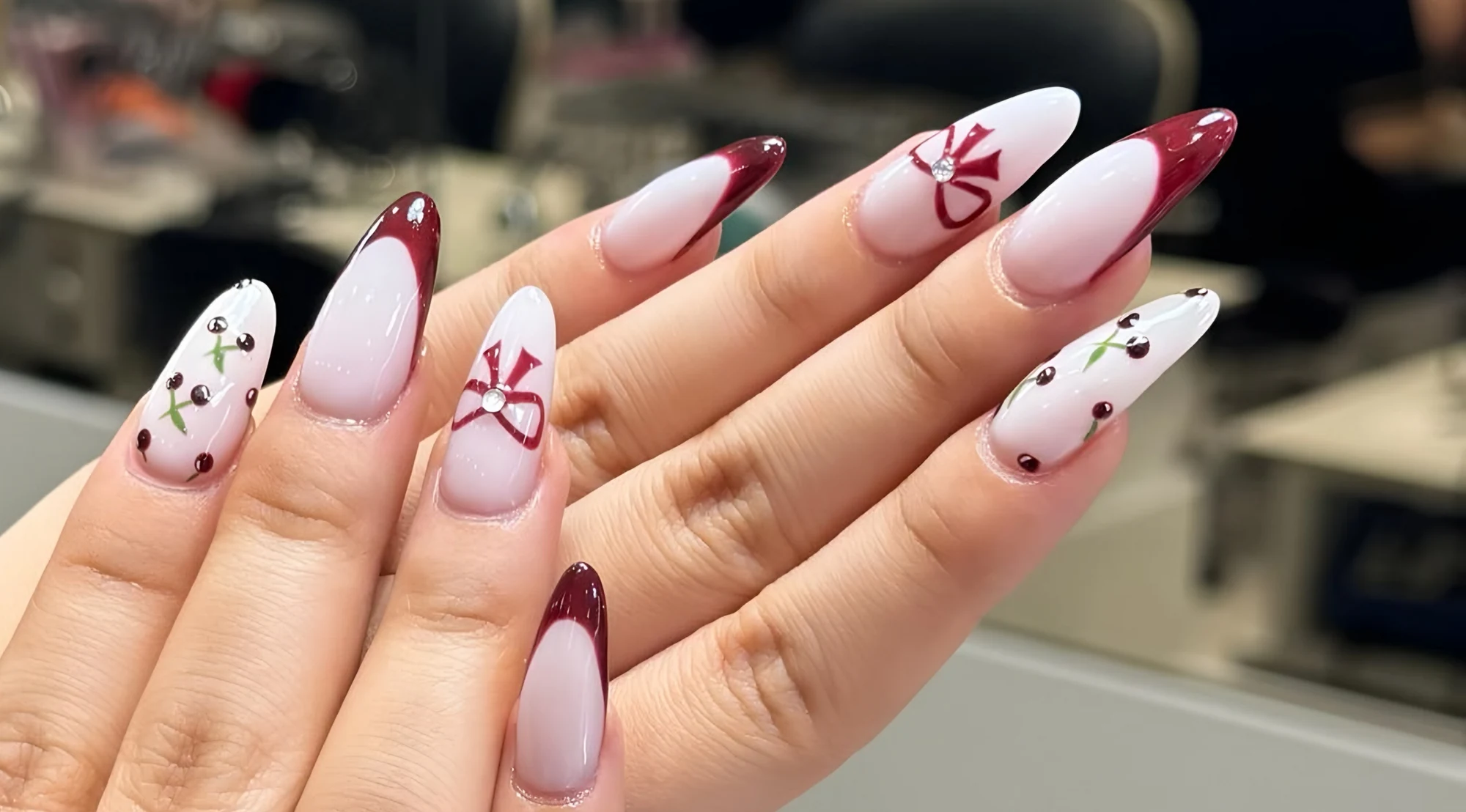 Wine-red French tips with painted bows, photographed inside the salon at Marrickville Metro